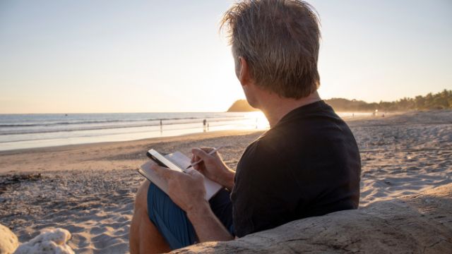 man sitting on a beach writing in journal
